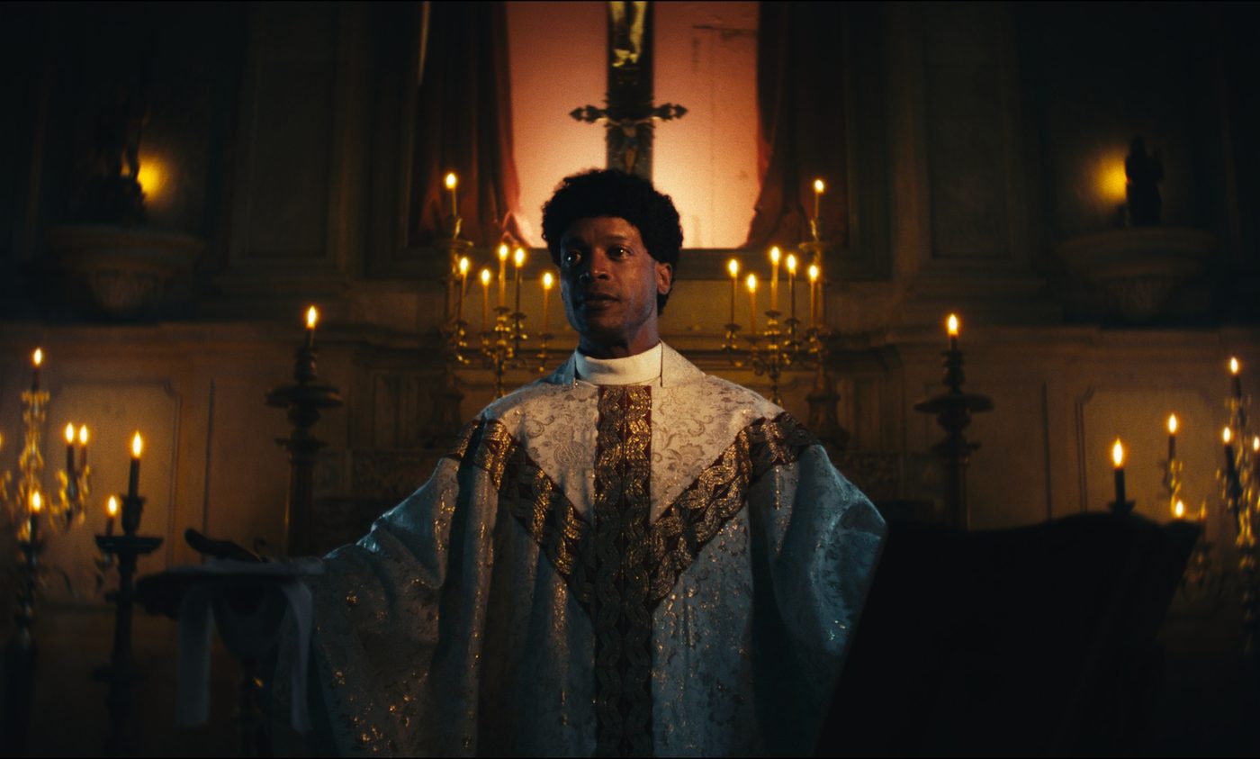 O padre diante do altar, de braços abertos, rodeado de velas
