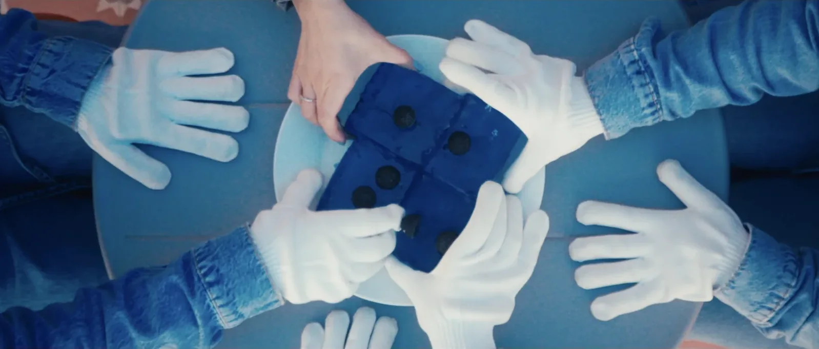 Mãos com luvas brancas à volta de uma mesa azul